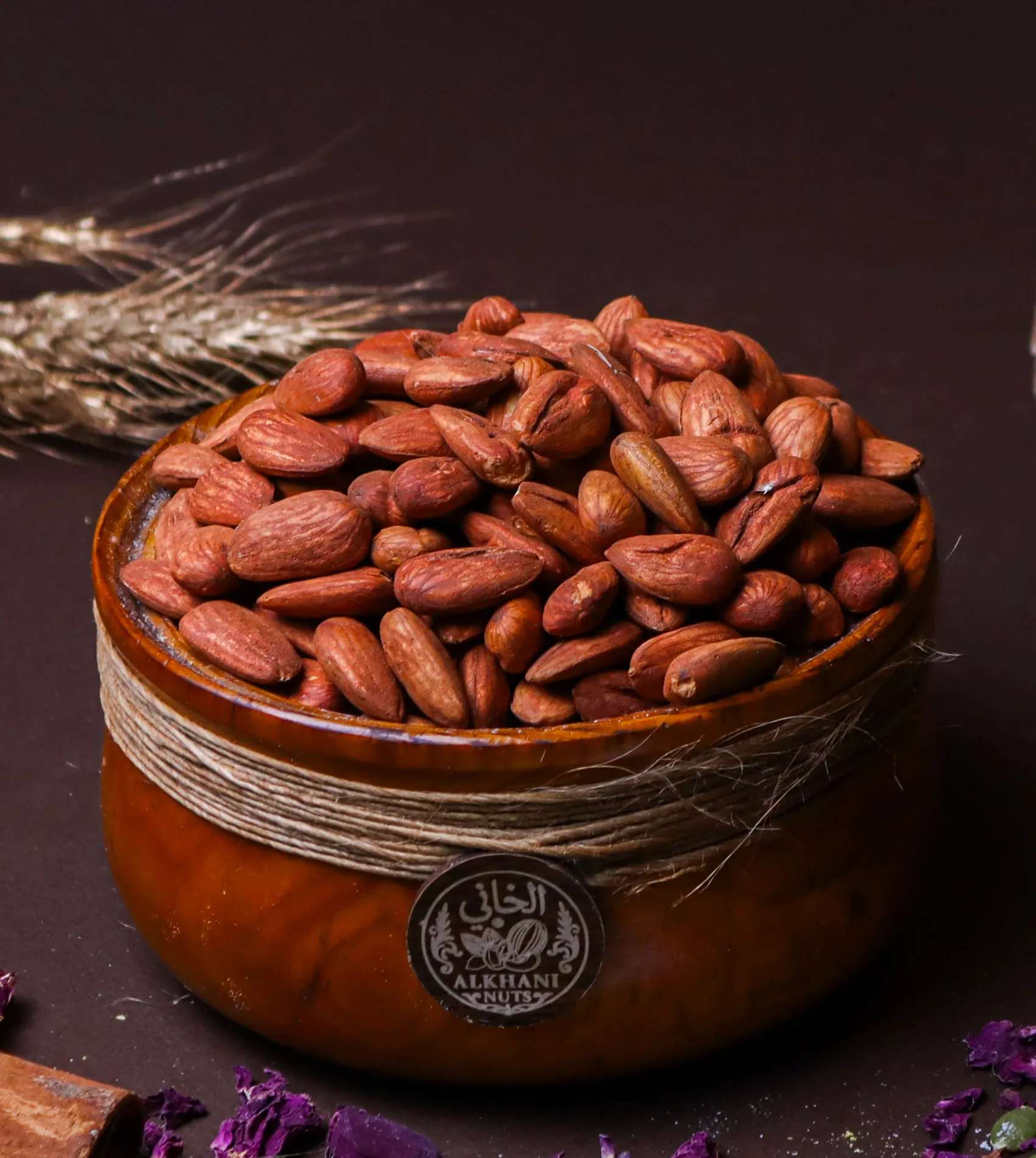 لوز محمّص مملّح، حبات كاملة بقشرتها البنية، بزبدية خشب ملفوفة بخيط خيش وعليها ختم الخاني