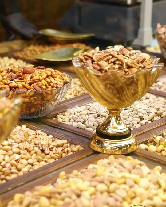 زبدية قزاز على رجل دهبية فوق صواني خشب مقسّمة فيها مكسرات، بفرع دمسكينو